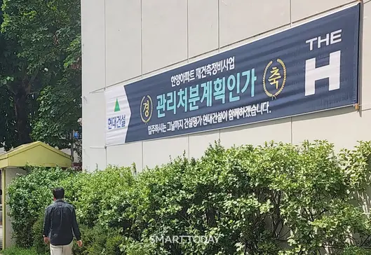 한 시민이 한양아파트 외벽에 부착된 현대건설 현수막을 보며 걷고 있다. 출처=김종현 기자