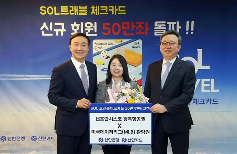 신한은행은 지난 15일 서울 중구 본점에서 SOL트래블 체크카드 50만 번째 발급 고객과 축하 기념식을 열었다. 정상혁 신한은행장(오른쪽)과 문동권 신한카드 사장(왼쪽)이 고객(가운데)에게 미국 샌프란시스코 왕복항공권과 미국 메이저리그(MLB) 관람권 금액에 상당하는 마이신한포인트를 전달했다. [출처: 신한은행]