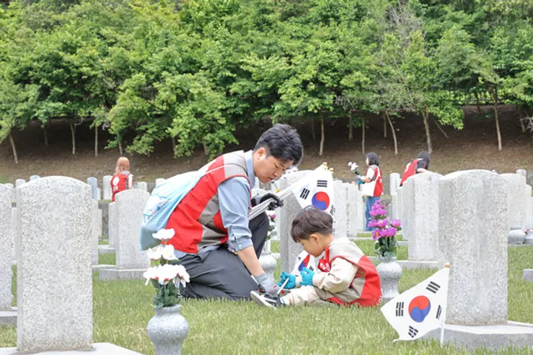 현충원 묘역단장 봉사활동에 참가한 롯데건설 임직원 가족이 묘비 옆에 태극기를 꼽고 있다.