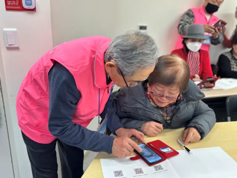 전년도 우수 수강생이자 올해 보조강사로 활동하는 어르신(왼쪽)이 ‘우리(WOORI) 어르신 IT 행복 배움교실’에서 수강생의 학습을 돕고 있다. [출처: 우리금융그룹]