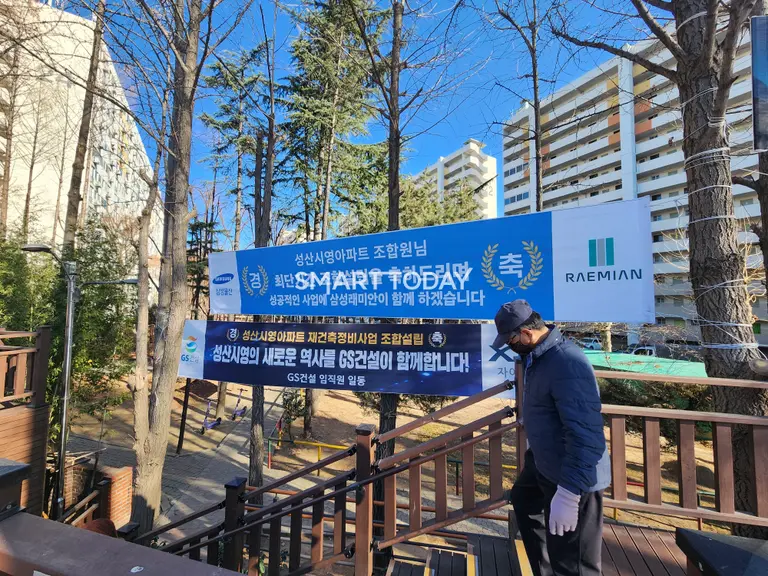 한 시민이 삼성물산과 GS건설의 홍보 플랜카드가 걸린 마포 성산시영아파트 단지 입구를 지나고 있다. 출처=김종현 기자 