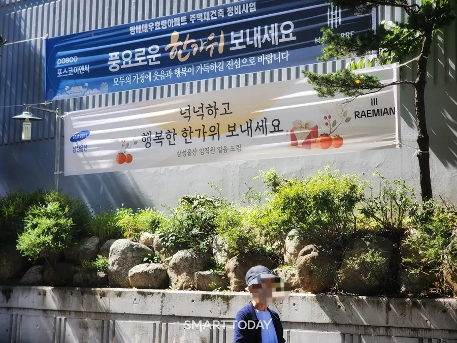 한 시민이 대우효령아파트 입구를 지나가고 있다. 아파트 외벽에 삼성물산과 포스코이앤씨의 현수막이 걸려 있다. 출처=김종현 기자